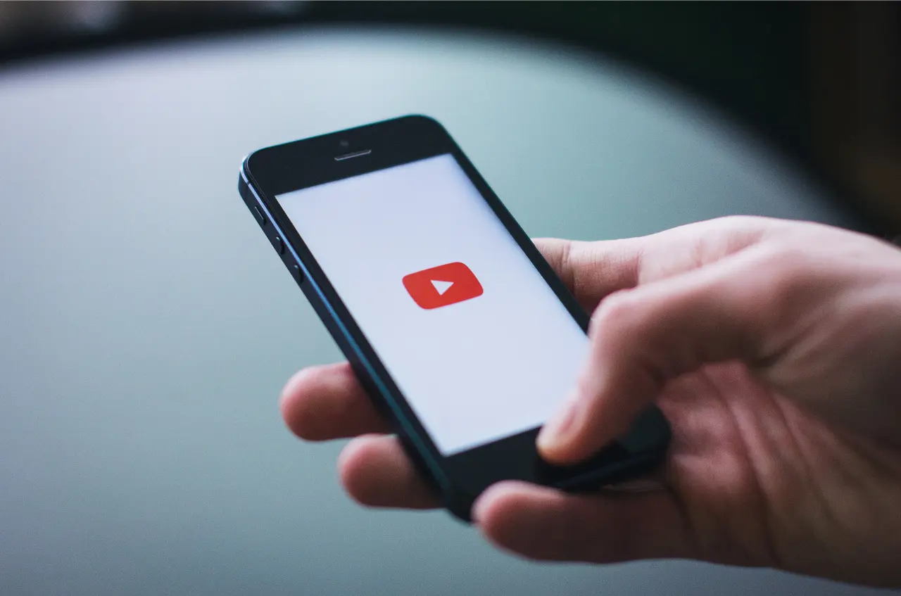 Dłoń trzymająca smartfon z wyświetlonym logo YouTube
